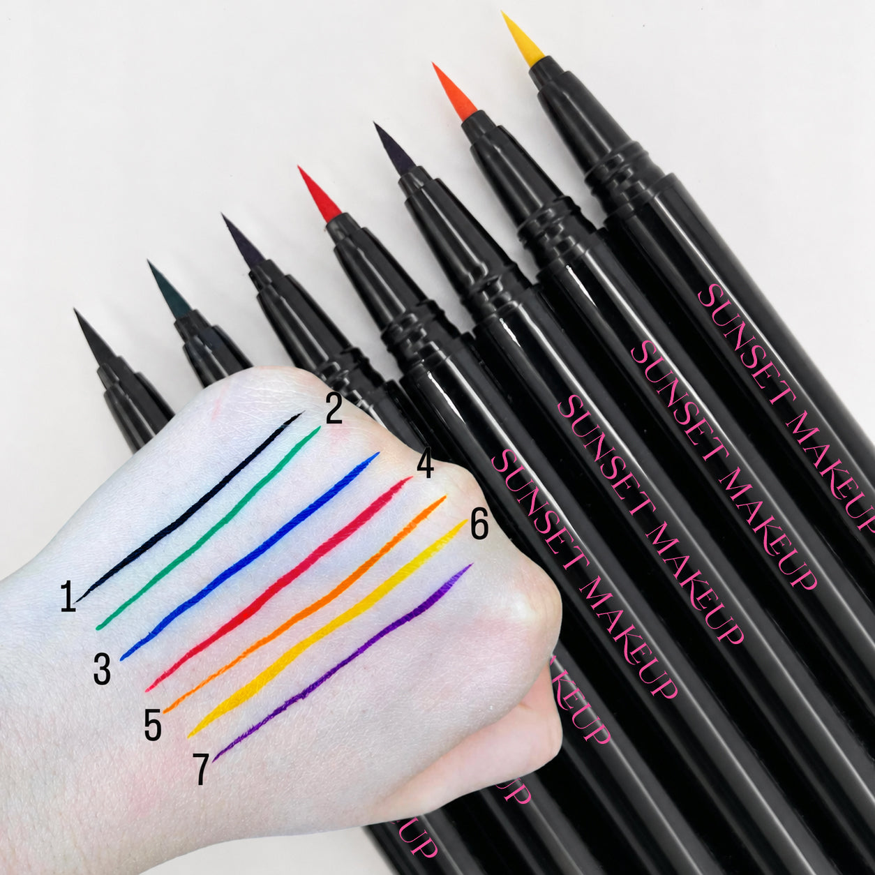 Sunset Makeup Seven cosmetic felt tip eyeliner pens arranged on a white background, with a hand showing numbered color swatches from each pen tip.