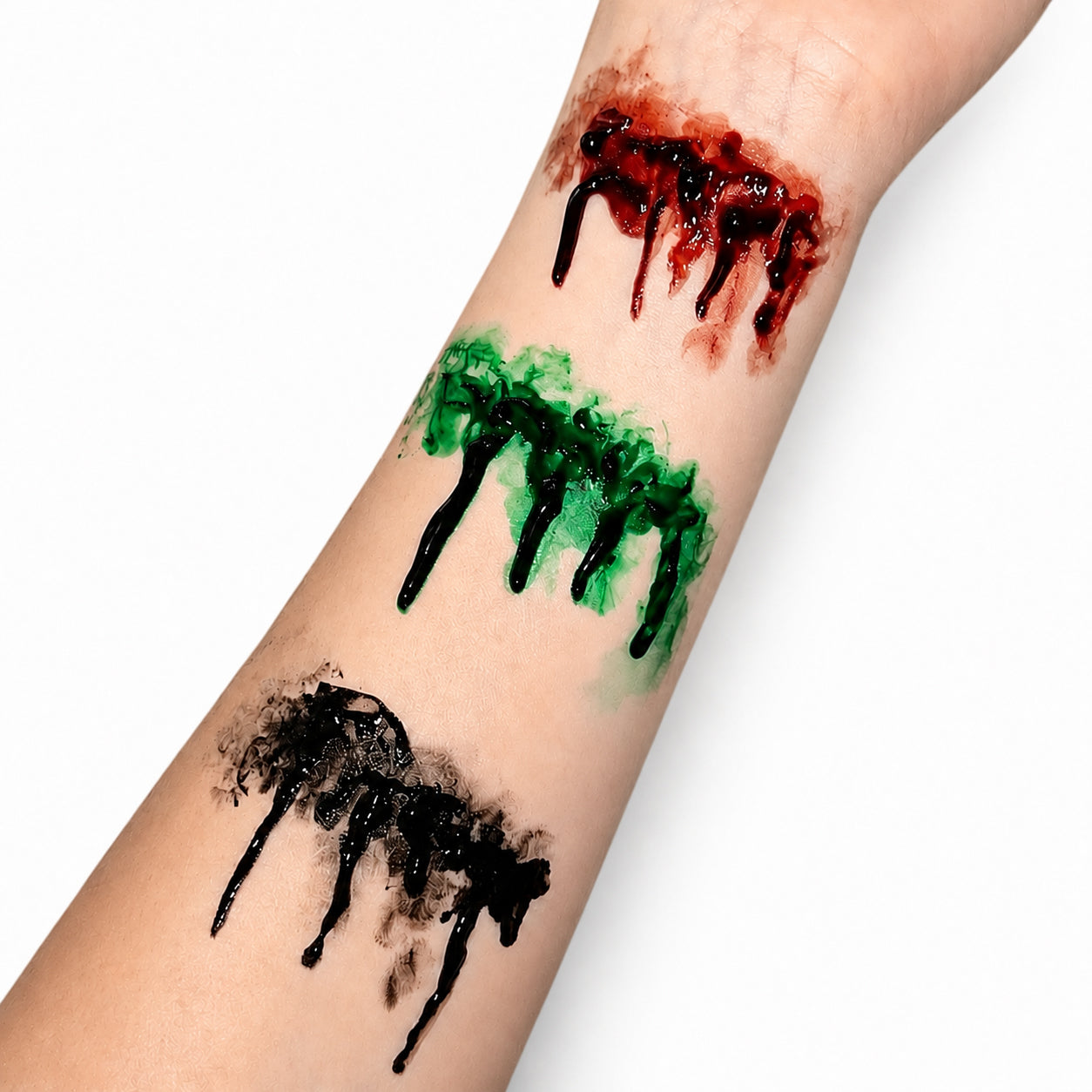 Three Halloween fake wound gels with dripping blood effects applied to a person's forearm, showing in red, green and black.