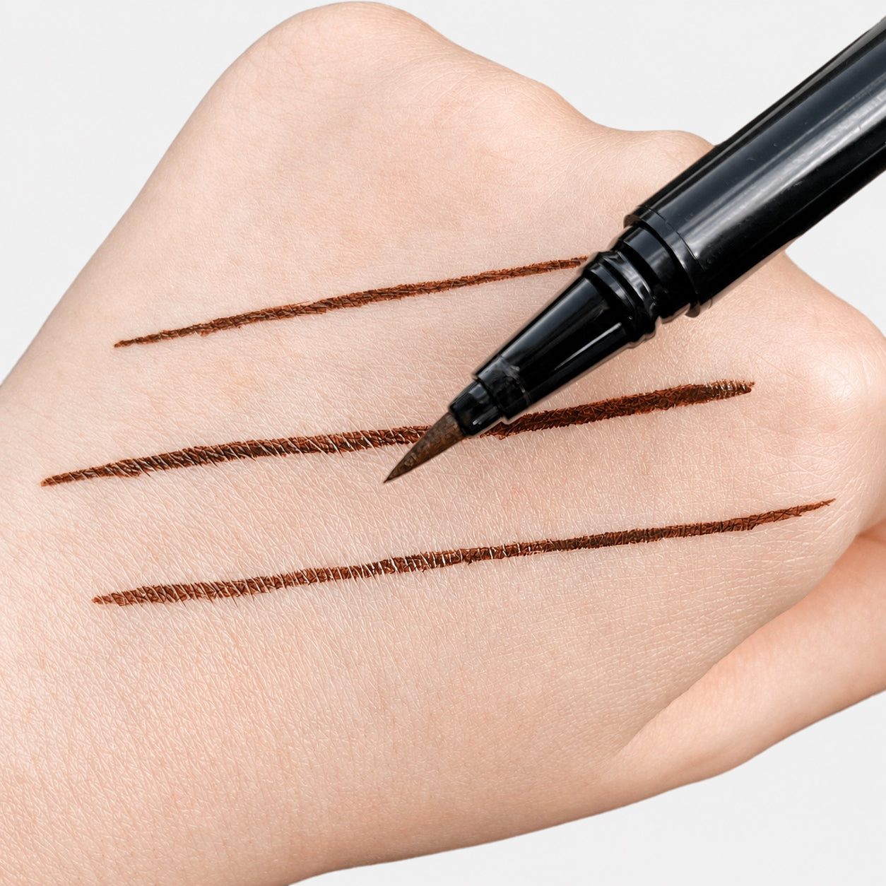 Sunset Makeup brown felt-tip eyeliner with three precise brown line swatches on a hand.