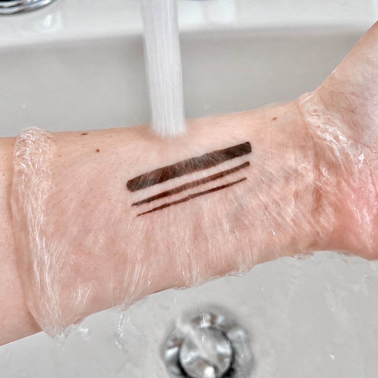Brown felt-tip eyeliner swatches under running water during a water-resistance test.