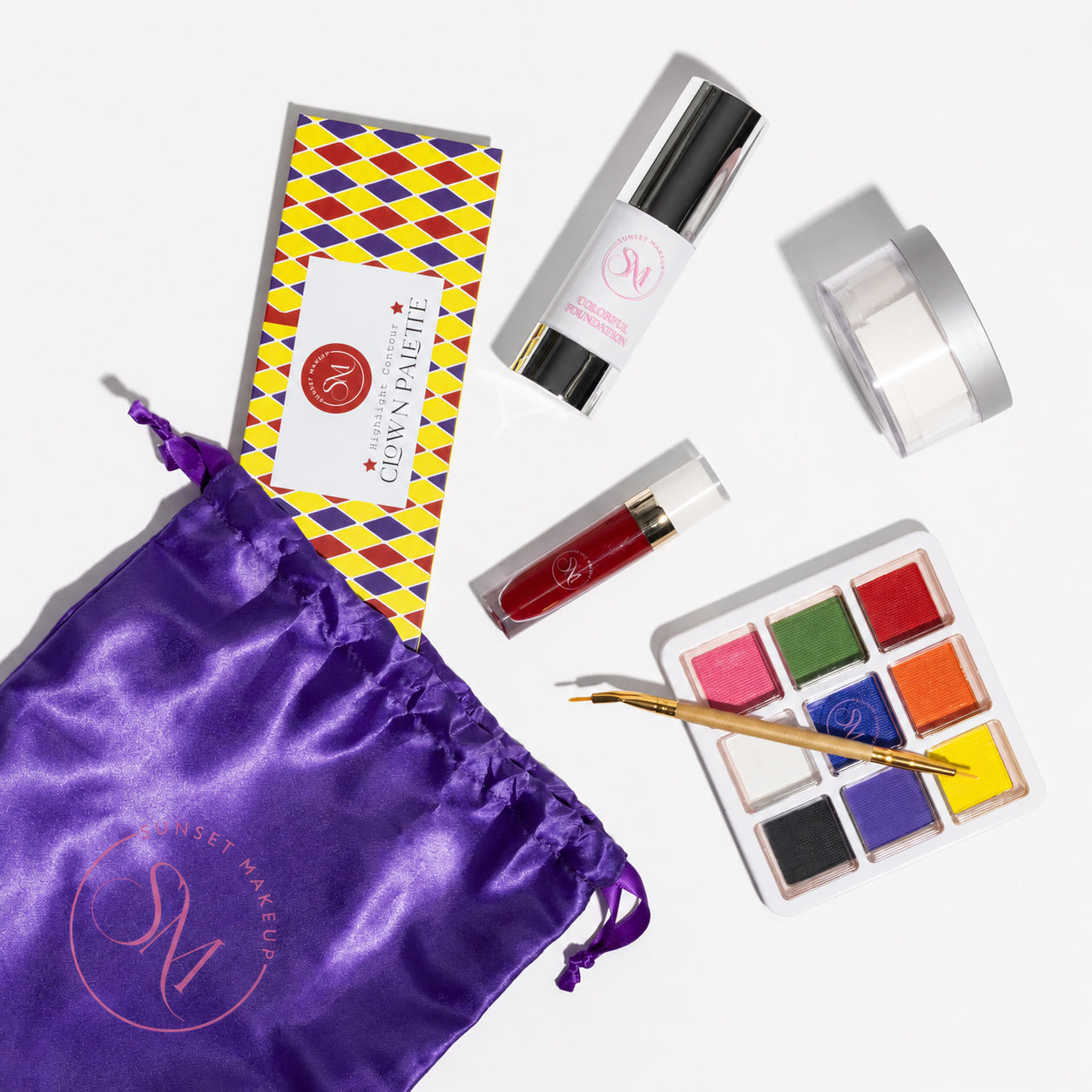 Sunset Makeup Clown Makeup Bundle with white foundation, translucent setting powder, colorful water activated eyeliner and face paint palette, red matte liquid lipstick, brush, and purple makeup bag.