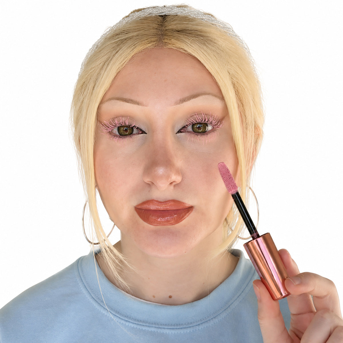 Model wearing pastel pink mascara on upper and lower lashes while holding the matching mascara wand against a white background.