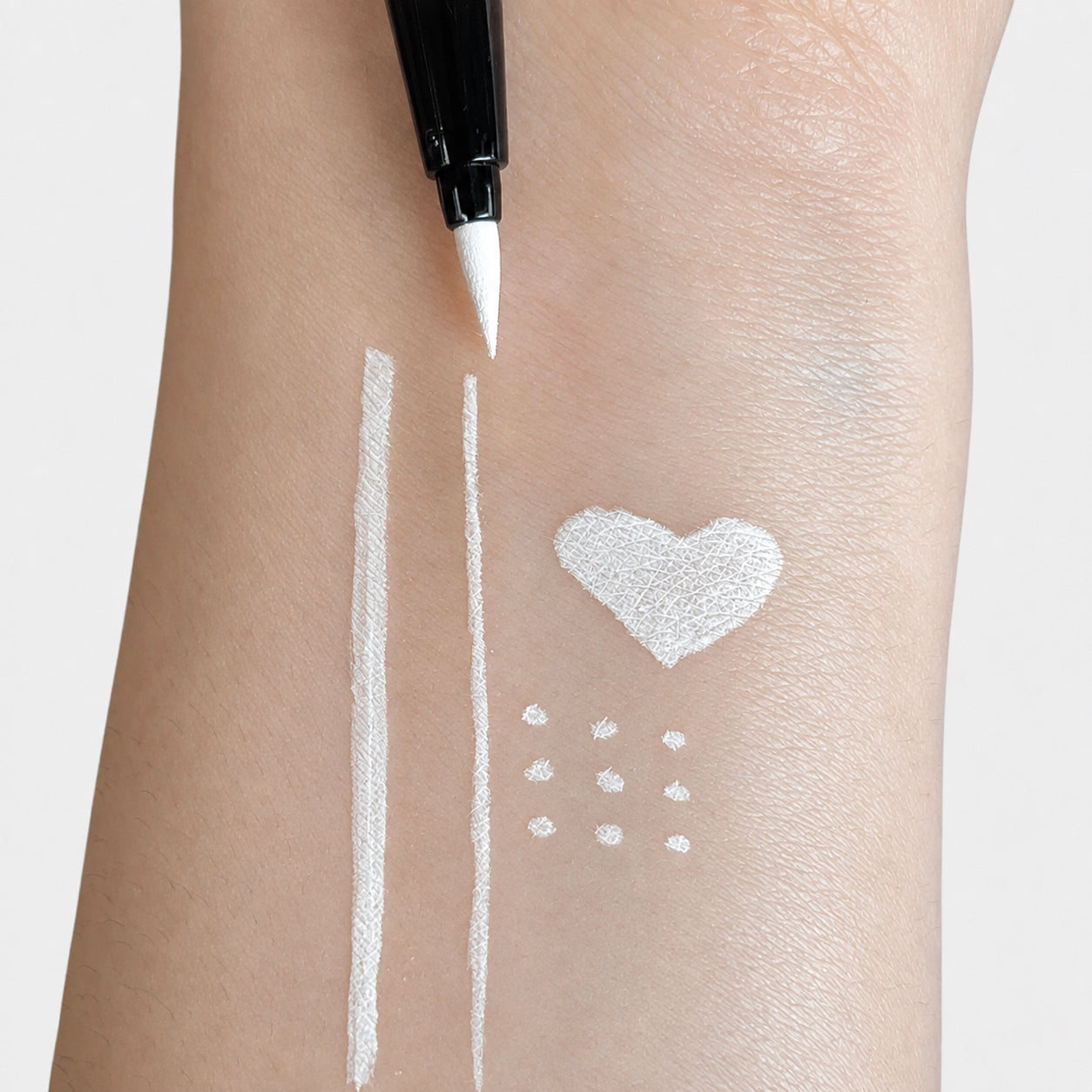 Sunset Makeup white felt-tip eyeliner creating opaque white lines, a heart, and dots on skin.
