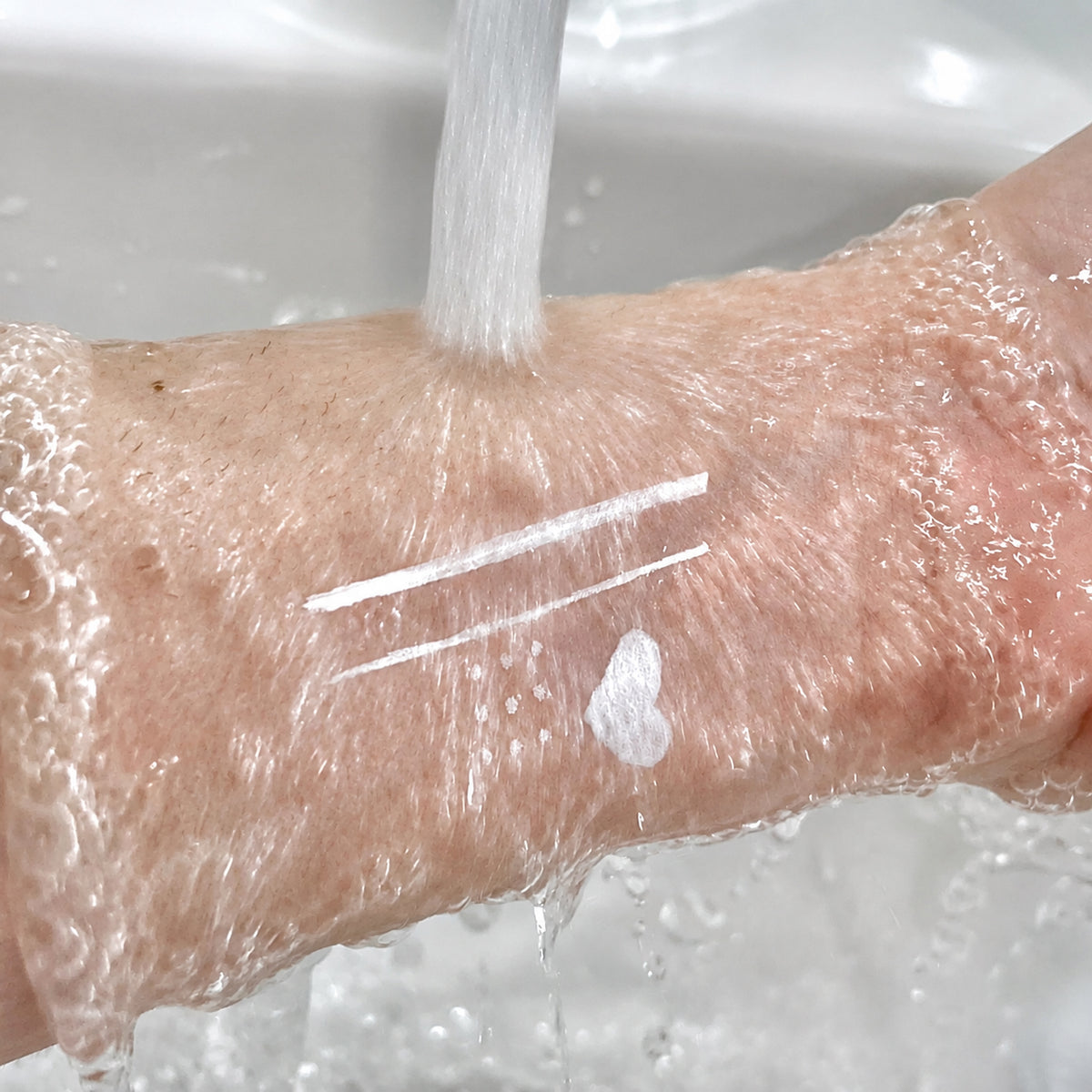 White felt-tip eyeliner lines, dots, and heart remaining visible under running water during a water-resistance test.
